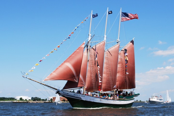 Sailing ship with red sails and flags on a sunny day, American flag on top, open sea.