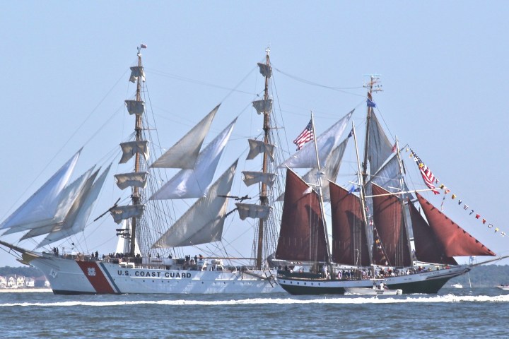 Two tall ships with sails unfurled sail side by side on open water.